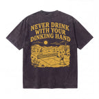 Black graphic T-shirt with yellow print of two people playing pickleball in a desert scene and text 'Never Drink With Your Dinking Hand'.