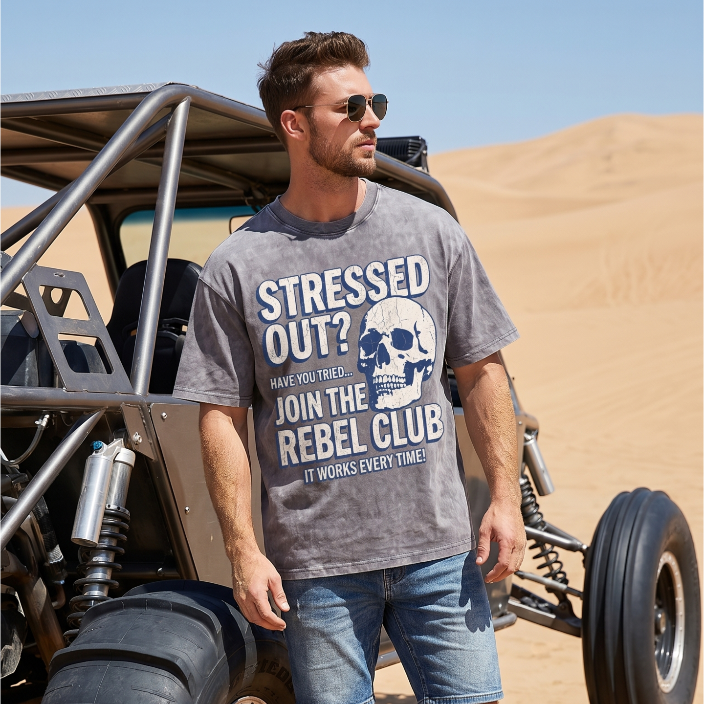 Man wearing graphic t-shirt with skull and rebel club print by dune buggy in desert