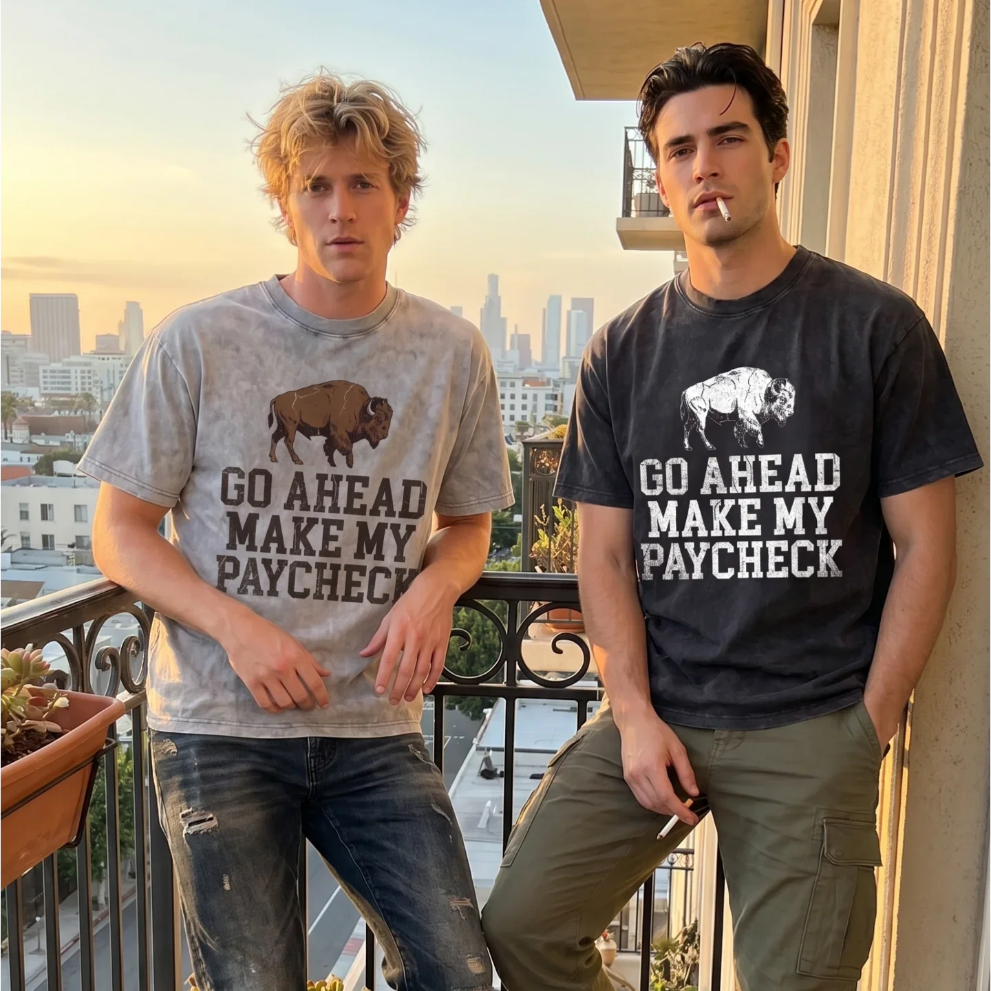 Two men wearing graphic t-shirts with 'Go Ahead Make My Paycheck' and buffalo print on a city balcony at sunset.